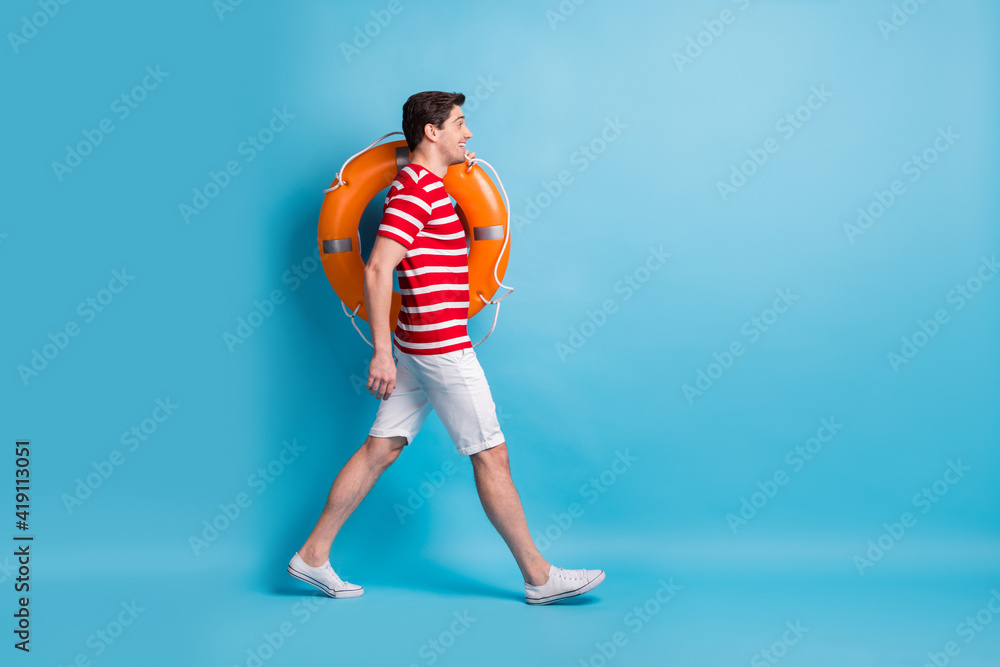 Full length body size side profile photo of guy cheerful walking with orange circle isolated on bright blue color background Full length body size side profile photo of guy cheerful walking with orange circle isolated on bright blue color background