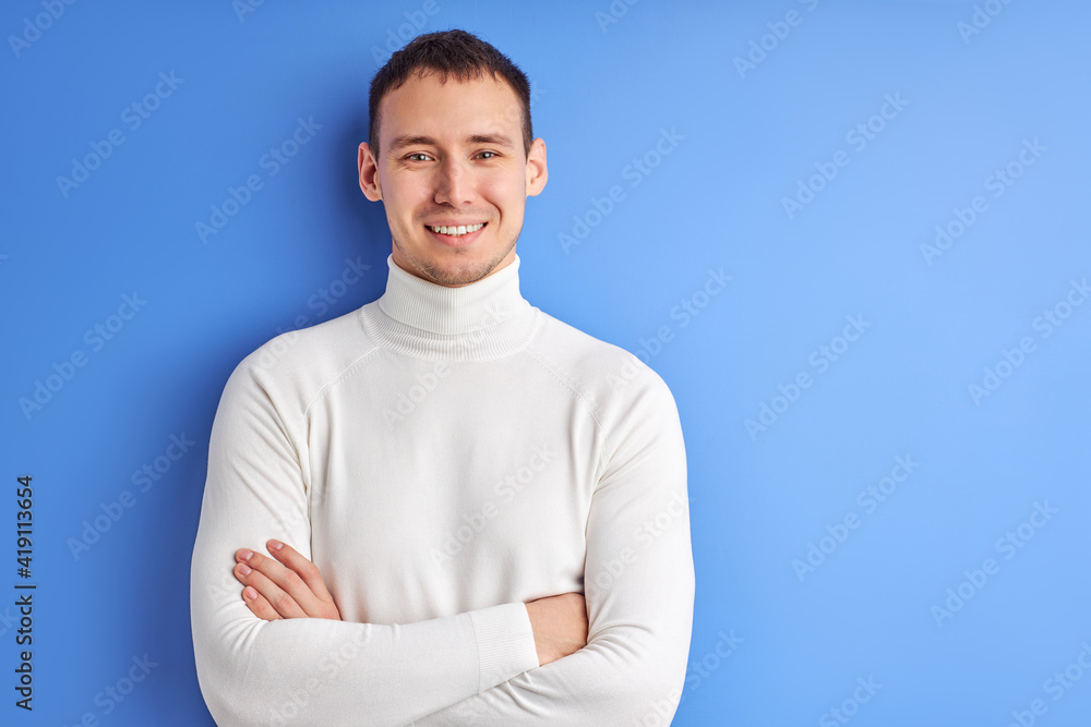 Portrait Of Male In Casual White Shirt Posing With Arms Folded, Smiling and Looking At Camera Isolated On Blue Background.