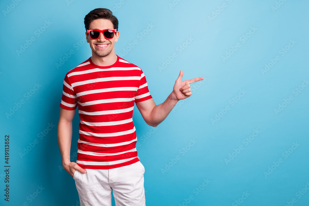 Photo portrait of young man smiling wearing stylish sunglass pointing promoting empty space isolated on vibrant blue color background Photo portrait of young man smiling wearing stylish sunglass pointing promoting empty space isolated on vibrant blue color background
