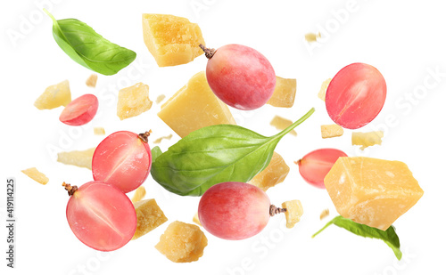 Fototapeta Naklejka Na Ścianę i Meble -  Pieces of delicious parmesan, grapes and basil leaves falling on white background