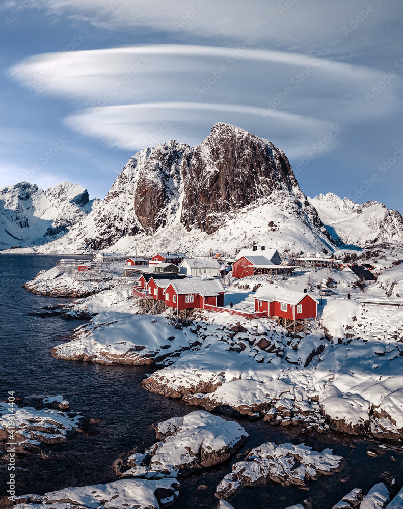 Wonderful wintry landscape. Impressive Winter scenery with Snowcapped mountain, traditional red fishing huts, rorbu and gorgeous sky with fairy tale clouds. Hamnoy village of an ideal resting place.