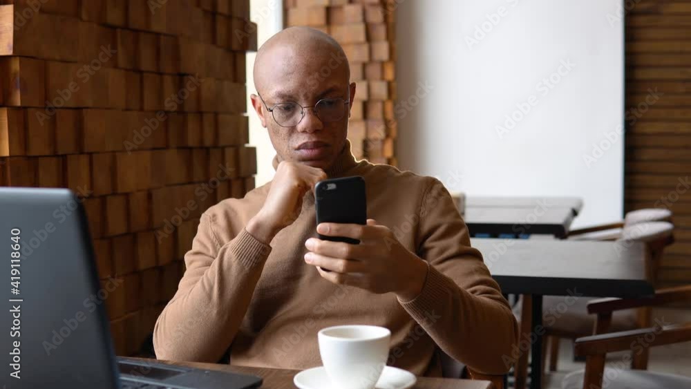 Serious young african working in a cafe using a smartphone Serious young african working in a cafe using a smartphone