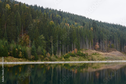 Beautiful lake view in the middle of mountains with green yellow orange red trees, reflected in water. Getaway vacation into natural surrounding. Mountain recreation. Low season in Bukovel ski resort