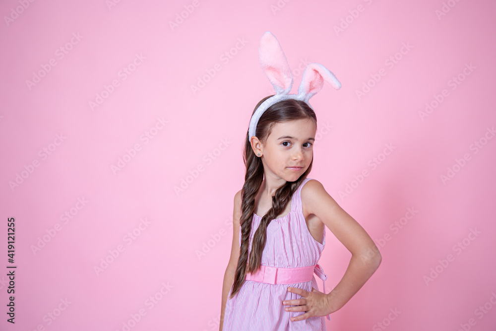 Little girl dressed in easter bunny ears and in a dress on a pink background copy space.