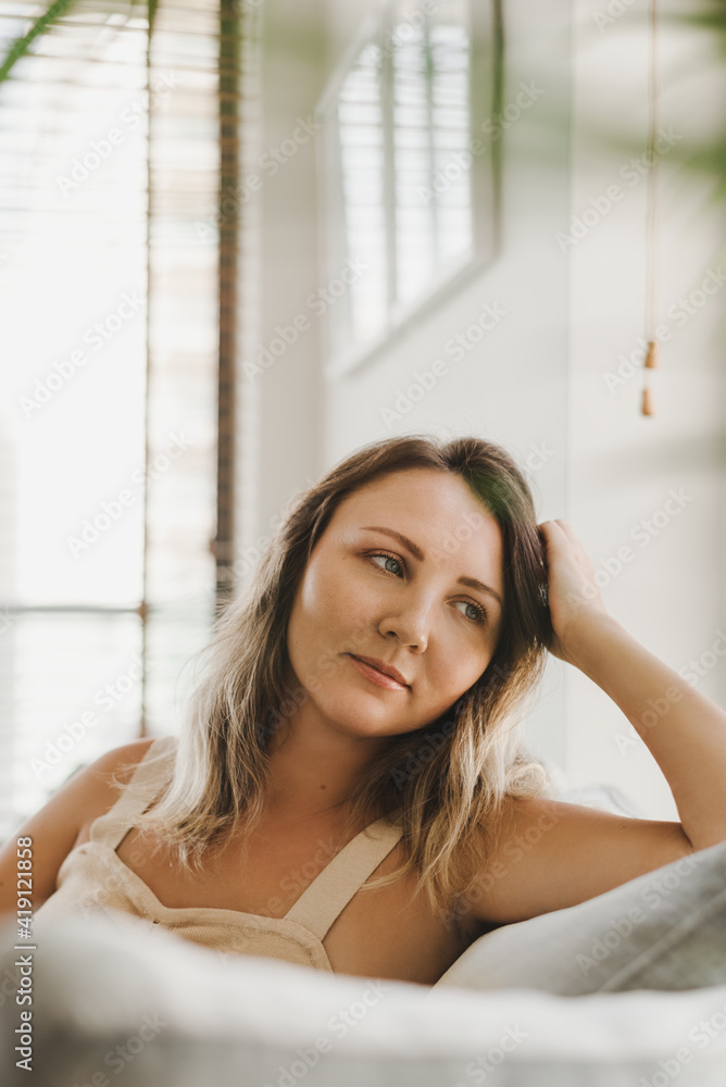 Portrait of a young woman sitting on a sofa at home. Casual style look. Coziness and comfort at home. Relaxing at home Portrait of a young woman sitting on a sofa at home. Casual style look. Coziness and comfort at home. Relaxing at home
