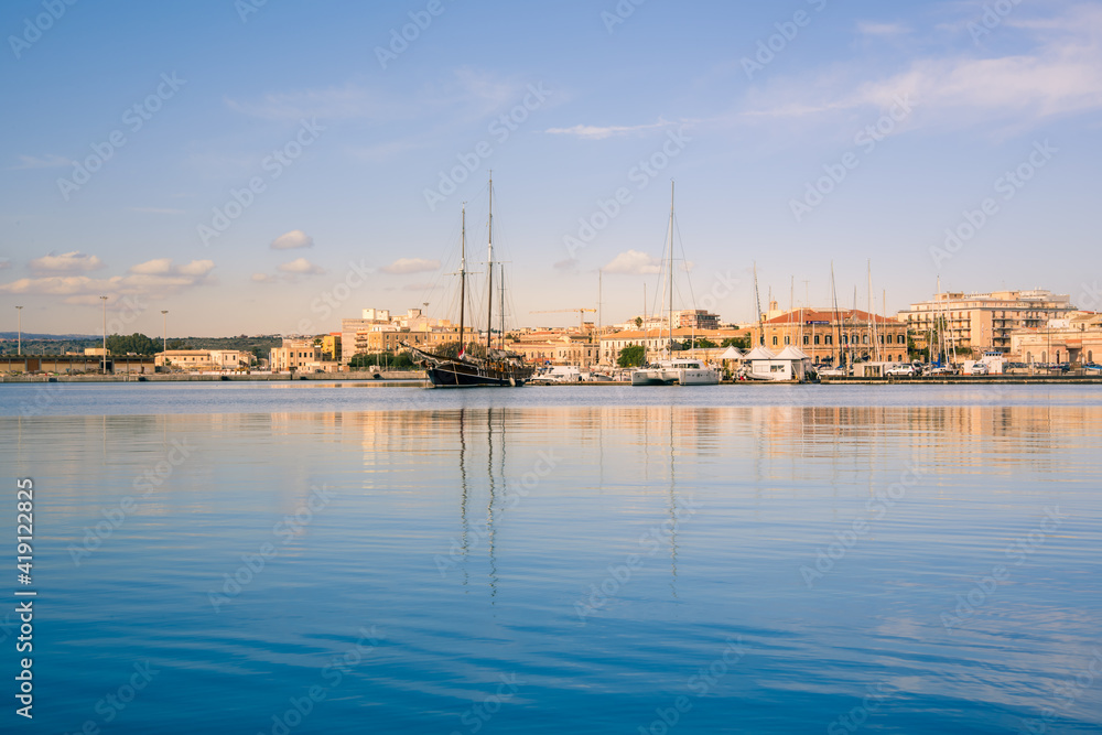 Ortigia, Syracuse, Italy / December 2018: Sailboats and yachts docked at the marina. Turquoise sea water, sunny sky, romantic Italian scenery