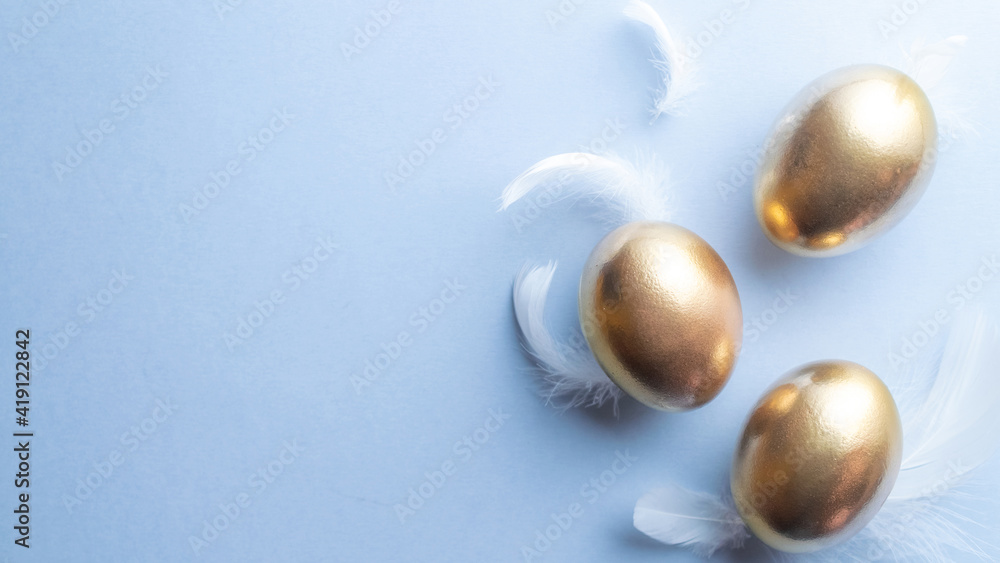 Golden easter colour eggs with white feathers on pastel blue background in Happy Easter decoration. Spring holiday top view concept. Golden easter colour eggs with white feathers on pastel blue background in Happy Easter decoration. Spring holiday top view concept.