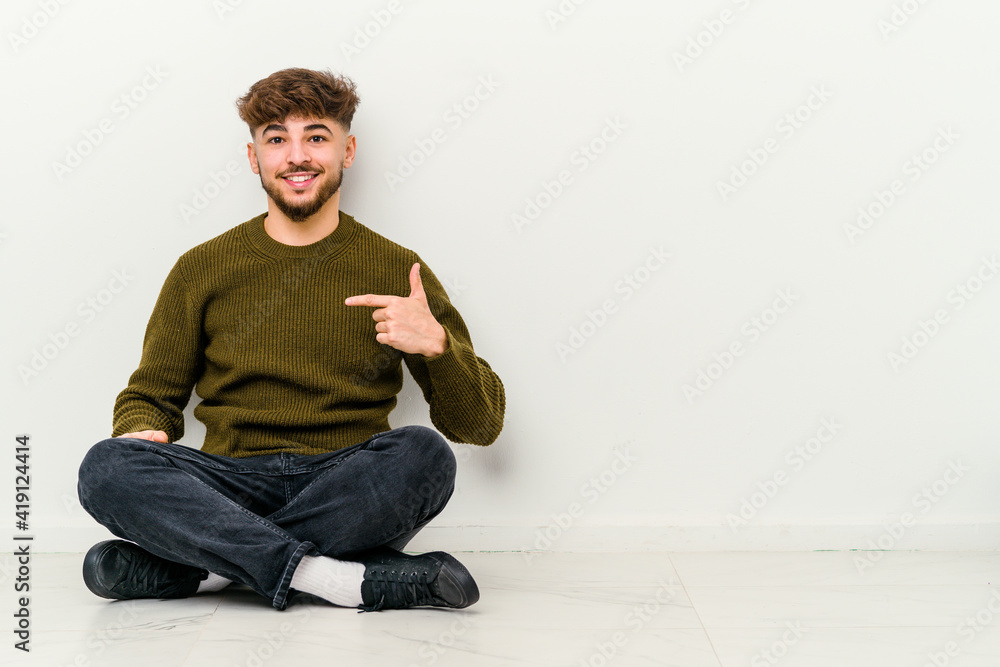 Young Moroccan man sitting on the floor isolated on white background person pointing by hand to a shirt copy space, proud and confident Young Moroccan man sitting on the floor isolated on white background person pointing by hand to a shirt copy space, proud and confident