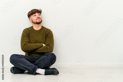 Young Moroccan man sitting on the floor isolated on white background dreaming of achieving goals and purposes © Asier