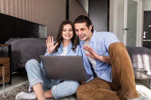Young couple video chatting sitting on floor at home in bedroom