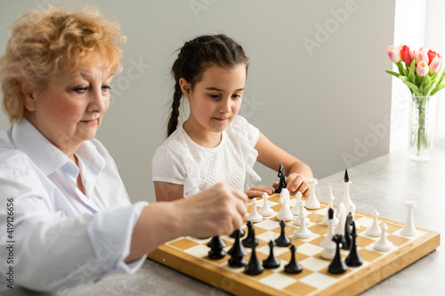 Young girl playing chess with grandmother together at home