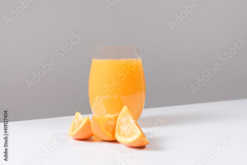 Jugo de naranja en un vaso de cristal con trozos de naranja sobre una mesa blanca con un fondo gris photo