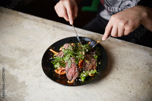 Man eating Steak Salad with Grilled Beef; arugula; carrot and seeds. Healthy food
