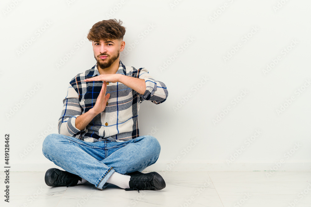 Young Moroccan man sitting on the floor isolated on white background showing a timeout gesture.