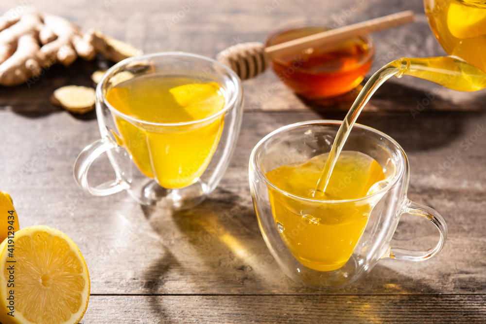 Pouring ginger tea with lemon and honey in crystal glass on wooden table Pouring ginger tea with lemon and honey in crystal glass on wooden table