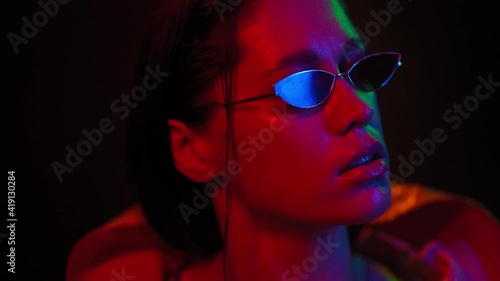 Pretty girl slow motion moving in neon light on black background. Beautiful girl dancing in lights wearing sunglasses. Art design of female disco dancing, Night club, Party. FHD footage. 