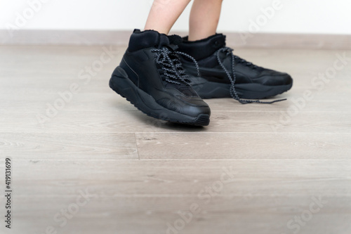 child s feet in large men s sneakers close-up on the laminate floor. sports and fitness
