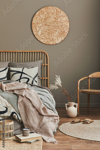 Stylish composition of bedroom interior with wooden bed, chair, carpet decro, stool, rattan decoration, vases and elegant accessories. Beautiful bed sheets, blanket and pillows. Cozy home decor. photo