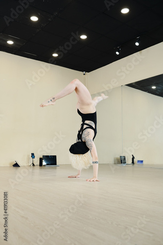 Fit strong woman in leotard doing handstand when training alone in studio with big mirrors