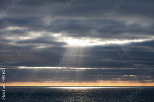 The sun bursts through dark storm clouds over the sea in Cornwall photo