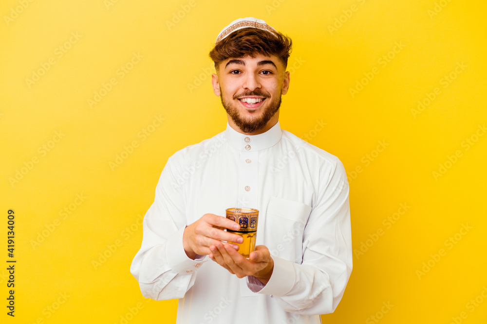 Young Moroccan man wearing the typical arabic costume drinking tea isolated on yellow background Young Moroccan man wearing the typical arabic costume drinking tea isolated on yellow background