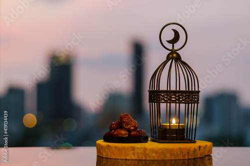 Lantern that have moon symbol on top and dates fruit put on wooden tray with city background for the Muslim feast of the holy month of Ramadan Kareem.
