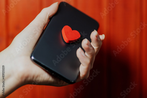 female hand holding a smartphone with a love heart. concept of long-distance relationship