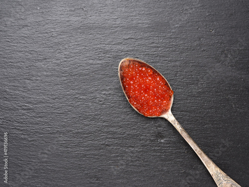 red caviar of chum salmon in a metal spoon on a black background