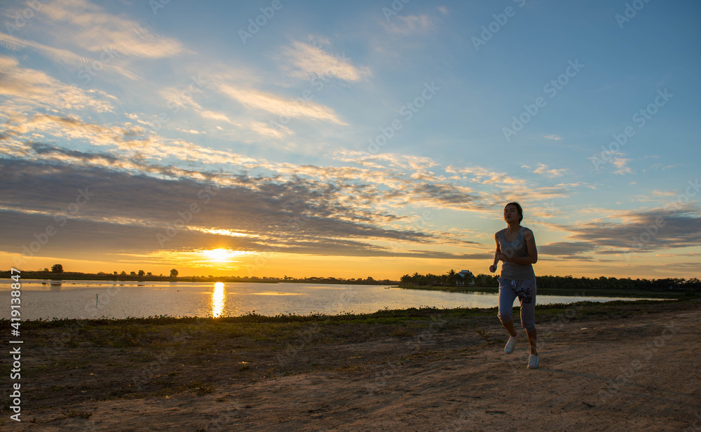 A Beautiful woman jogging in the morning above the dam at the sky sunset.
