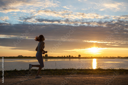 A Beautiful woman jogging in the morning above the dam at the sky sunset.