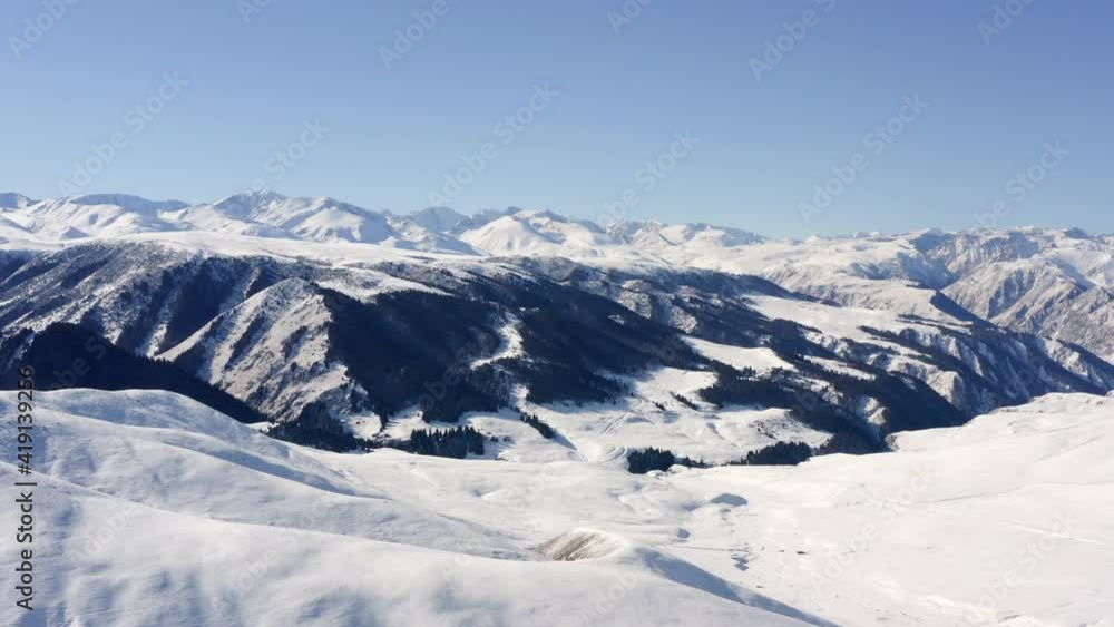 Drone video of winter mountains in a beautiful landscape. Forests with pines on the slopes of the mountains are covered with snow. Peaks and mountain ranges in sunny weather with blue sky. Drone video of winter mountains in a beautiful landscape. Forests with pines on the slopes of the mountains are covered with snow. Peaks and mountain ranges in sunny weather with blue sky.