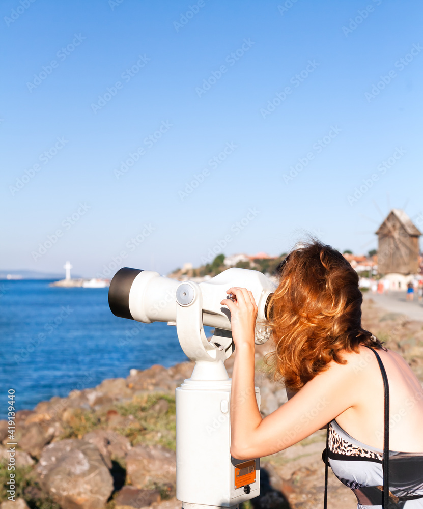 Young woman looking through binocular viewer on the sea landscape. Bulgaria. Nesebar. Black Sea coast.