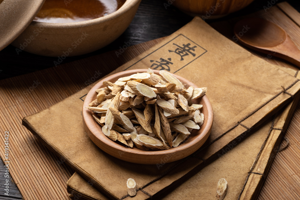 Fototapeta premium Astragalus membranaceus，Ancient Chinese medicine books and herbs on the table.English translation：Emperor's Internal Classic