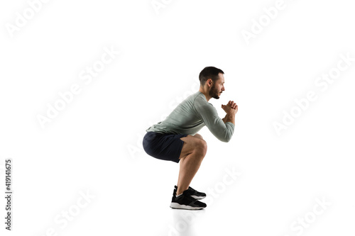 Squats. Young caucasian male model in action, motion on white background with copyspace. Concept of sport, movement, energy and dynamic, healthy lifestyle. Training, practicing. Authentic.