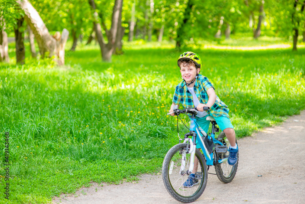 A boy with a green bicycle helmet on his head rides his bicycle in the summer park. Summer rest A boy with a green bicycle helmet on his head rides his bicycle in the summer park. Summer rest