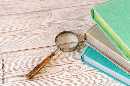 An old magnifying glass and a stack of books on a wooden table. The concept of getting knowledge from books. Selective focus.