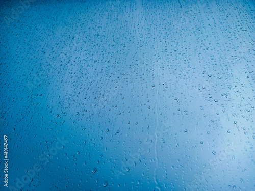 Raindrops on a window pane close-up. Abstract blue background.