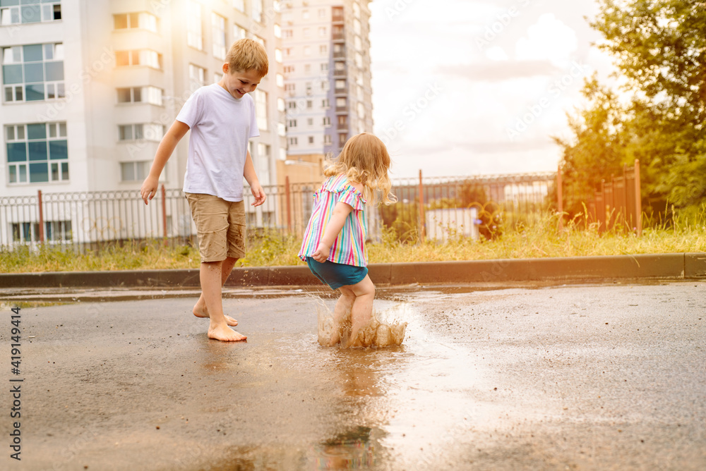 brother and sister running barefoot together in shallow puddle after ...