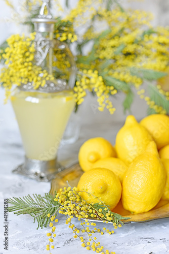 Lemons, yellow spring mimosa flowers and a decanter of lemon drink. Spring fresh still life. very soft selective focus in the foreground.