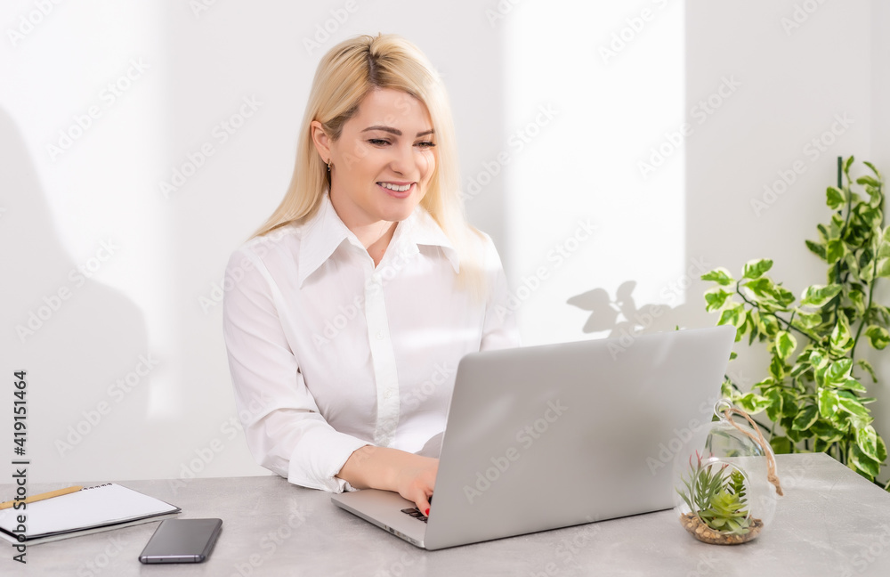 Portrait of a businesswoman using laptop in office against a white wall Portrait of a businesswoman using laptop in office against a white wall