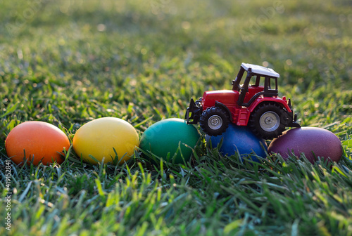 model of a toy red tractor, eggs painted in rainbow colors lie on the grass. Business concept of Easter greetings for farms. postcard. copy space