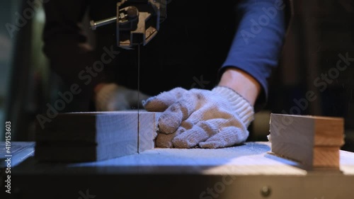 Close-up of a carpenter wearing protective gloves and a band saw. A master carpenter carves a piece for wood furniture. Home furniture production. Woodworking, needlework. Cold light