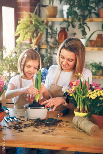 Cute child girl helps her mother to care for plants. Mom and her daughter engaged in gardening. Happy family in spring day.
