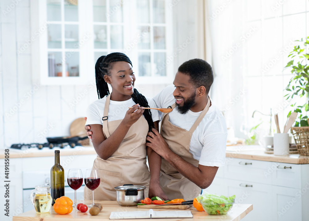 Joyful Black Spouses Tasting Food While Cooking Lunch In Kitchen
