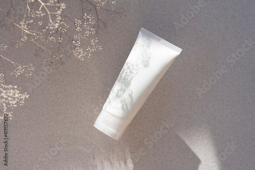  white cosmetic tube for face, hand or body cream with plant shadow on sunlit background.