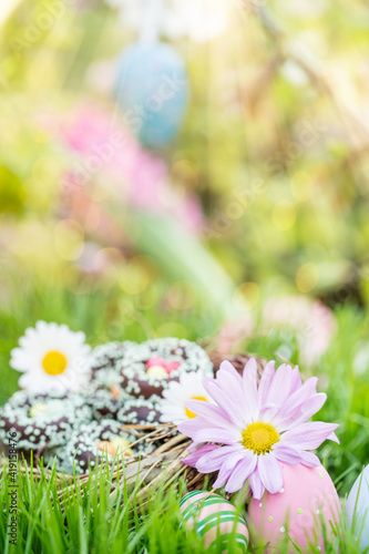 Beautiful chocolate Easter basket with colorful Easter eggs in the meadow in spring landscape in the garden. Trees in background and blur. Postcard. photo