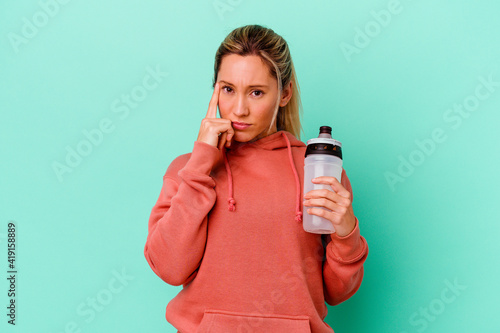 Young caucasian sport woman drinking water isolated on blue backgroundpointing temple with finger, thinking, focused on a task.