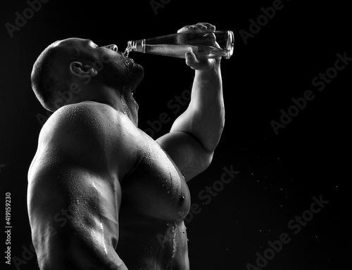 Young muscular build man silhouette drinking water from the bottle after running or after workout outdoors, fitness and healthy lifestyle concept on black background 