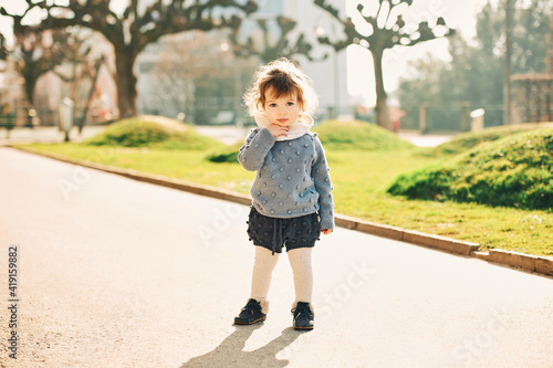 Outdoor portrait of adorable 1 - 2 year old toddler girl , wearing knitted pullver and shorts, playing in park © annanahabed