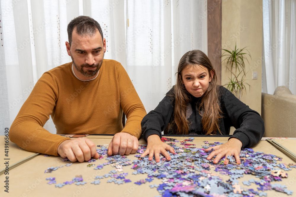 Concentrated father and daughter trying to put together a complicated puzzle of small pieces Concentrated father and daughter trying to put together a complicated puzzle of small pieces